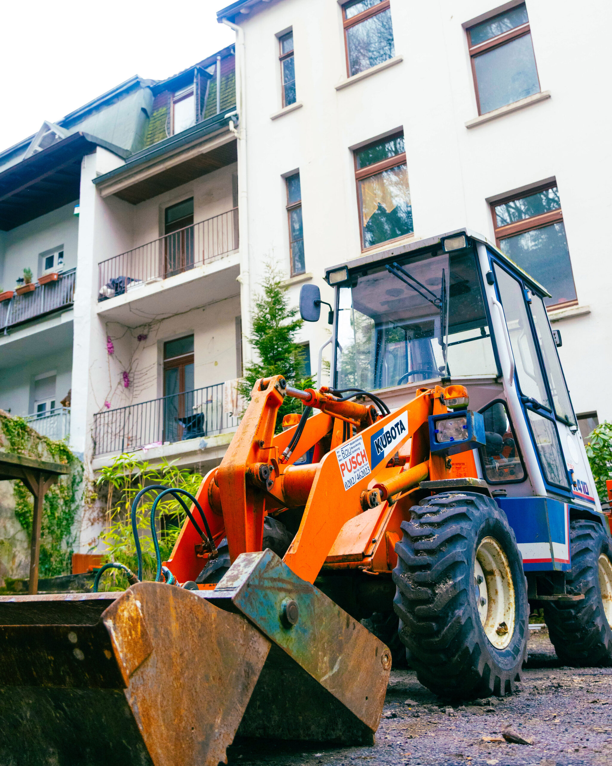 Foto von einem Bagger mit der Aufschrift "Pusch Bau". Der Bagger steht vor einer Immobilie.